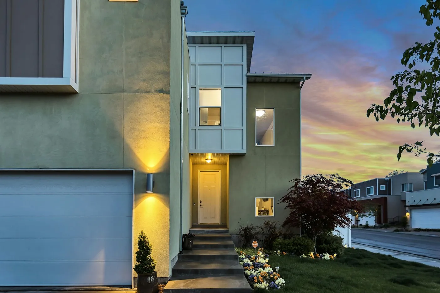 A modern home at twilight with warm light washing up the facade and over the entry, no seasonal decoration in sight.